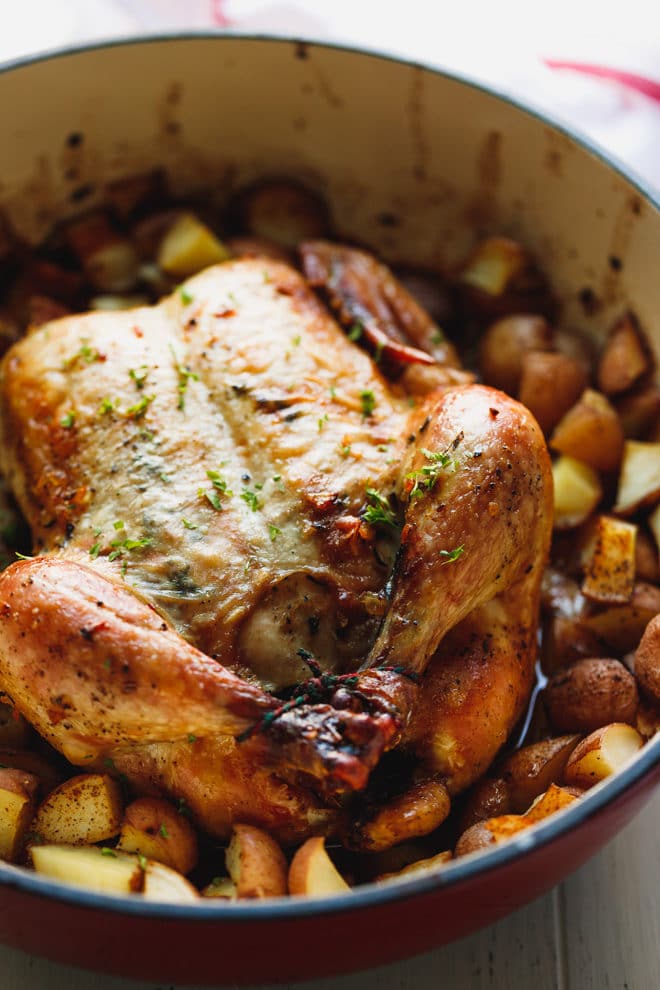 Whole roasted chicken with potatoes with golden skin in a baking dish