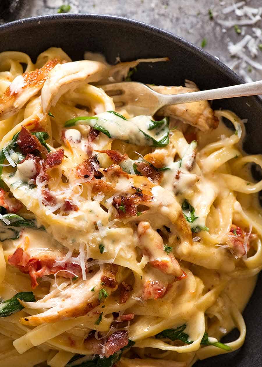 Close up of Chicken Pasta recipe with creamy alfredo sauce, sun dried tomato, spinach and bacon in a rustic black bowl, ready to be eaten
