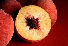 Photograph showing a peach in cross section with yellow flesh and a single large reddish brown pit