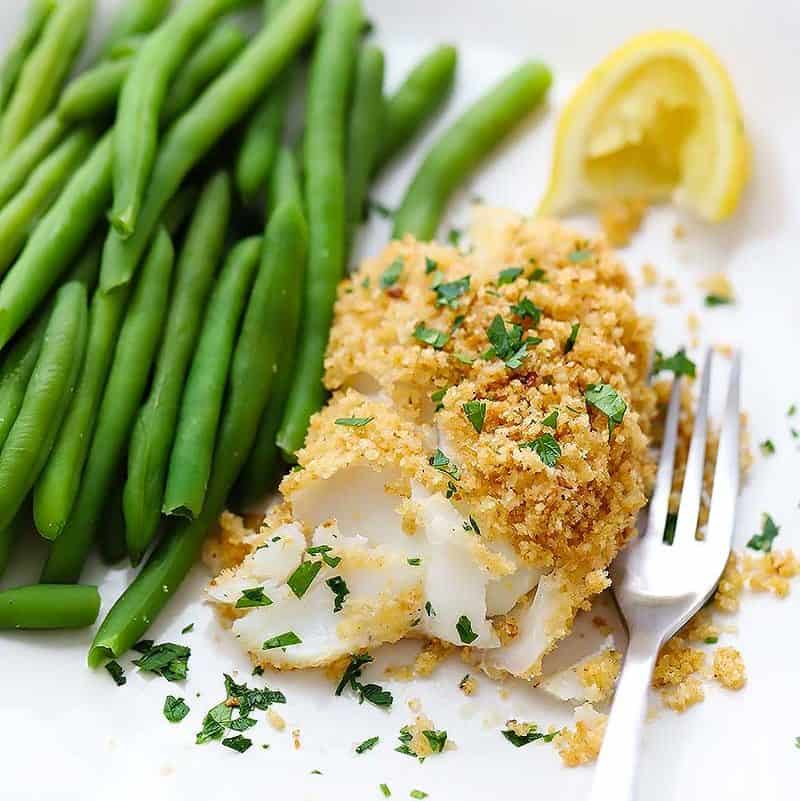 New England Baked Haddock on a plate with green beans, a lemon, and a fork