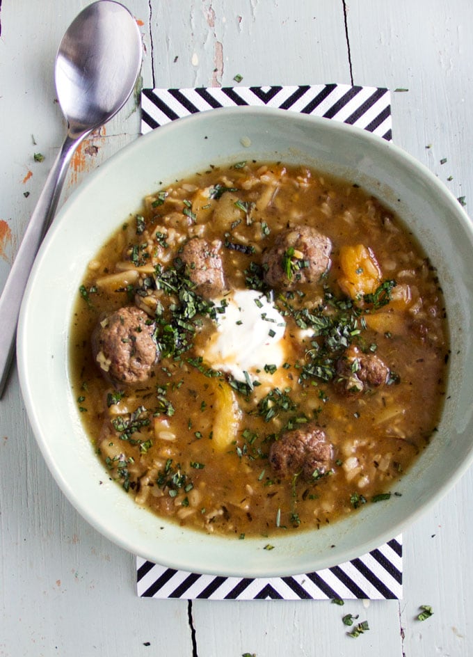 A light green bowl of meatball soup with a dollop of yogurt and a garnish of chopped herbs