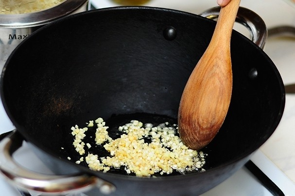 измельченные имбирь и чеснок в сковороде с маслом и деревянной лопаткой на плите